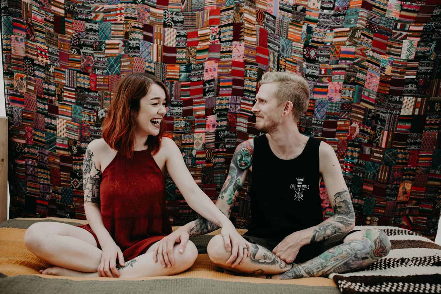 This Is the Boudoir Photography Shy Couples Need To See: Tattooed Couple Sits In Front of A Cozy Quilt
