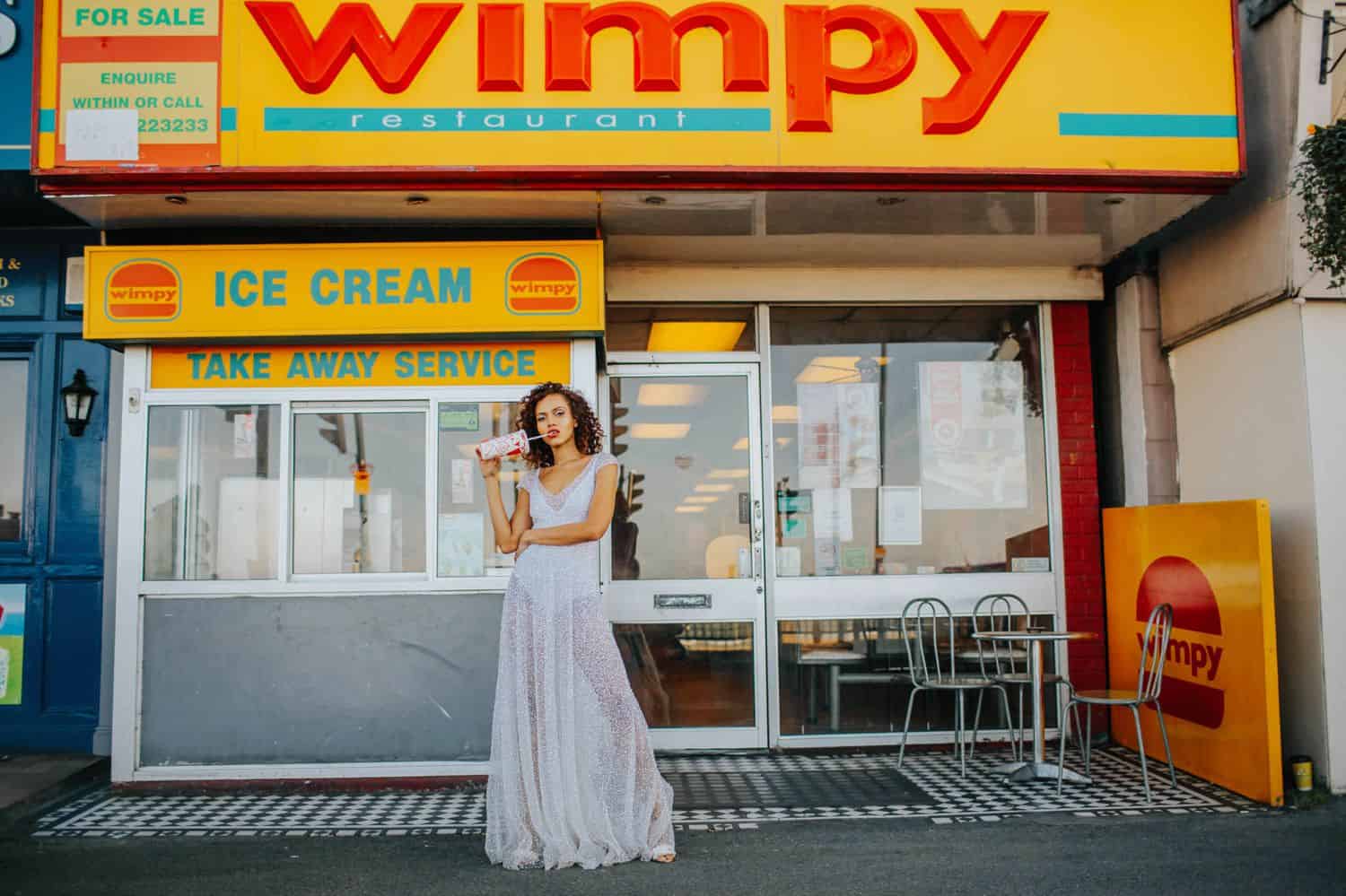 How To Make A Photography Website Your Dream Clients Can’t Resist: A woman in a sheer, glittery dress sips a milkshake in front of a takeaway counter.
