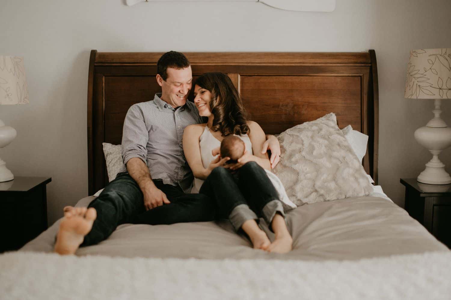 Learn to make lifestyle newborn photos like this one, with the parents sitting on their bed with their newborn in their laps.