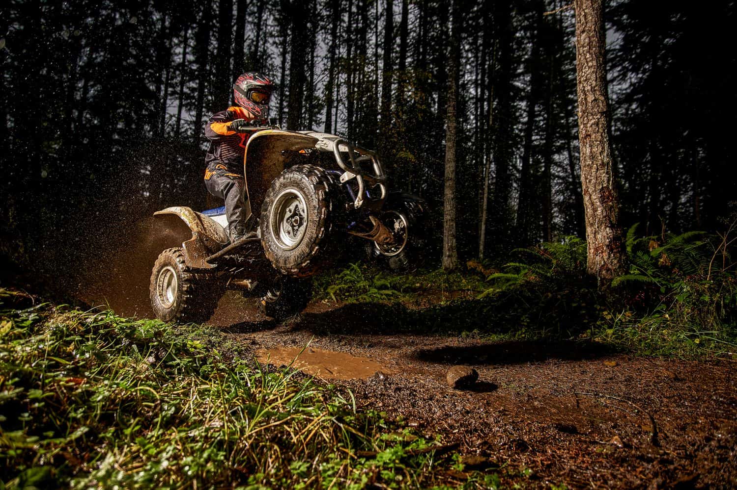 A high school senior boy rides his four-wheeler down a muddy road through the woods