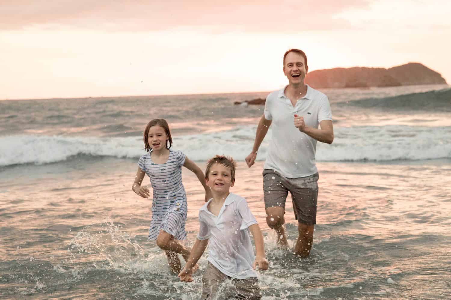 Dad and kids running in the ocean at sunset.