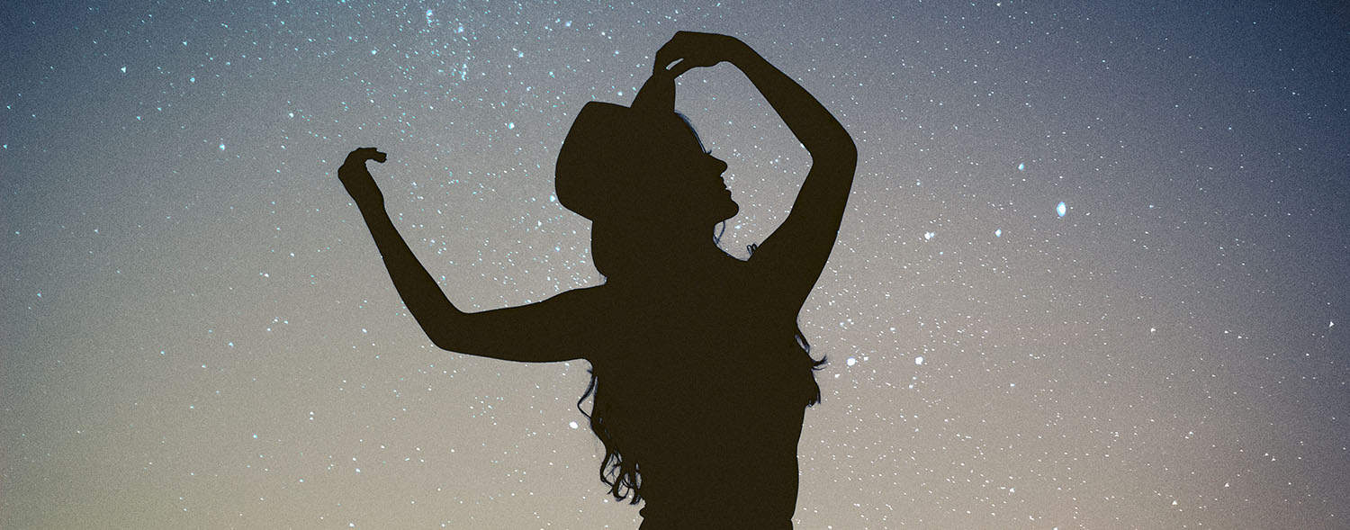 Silhouette of a woman standing in front of the night sky with stars.
