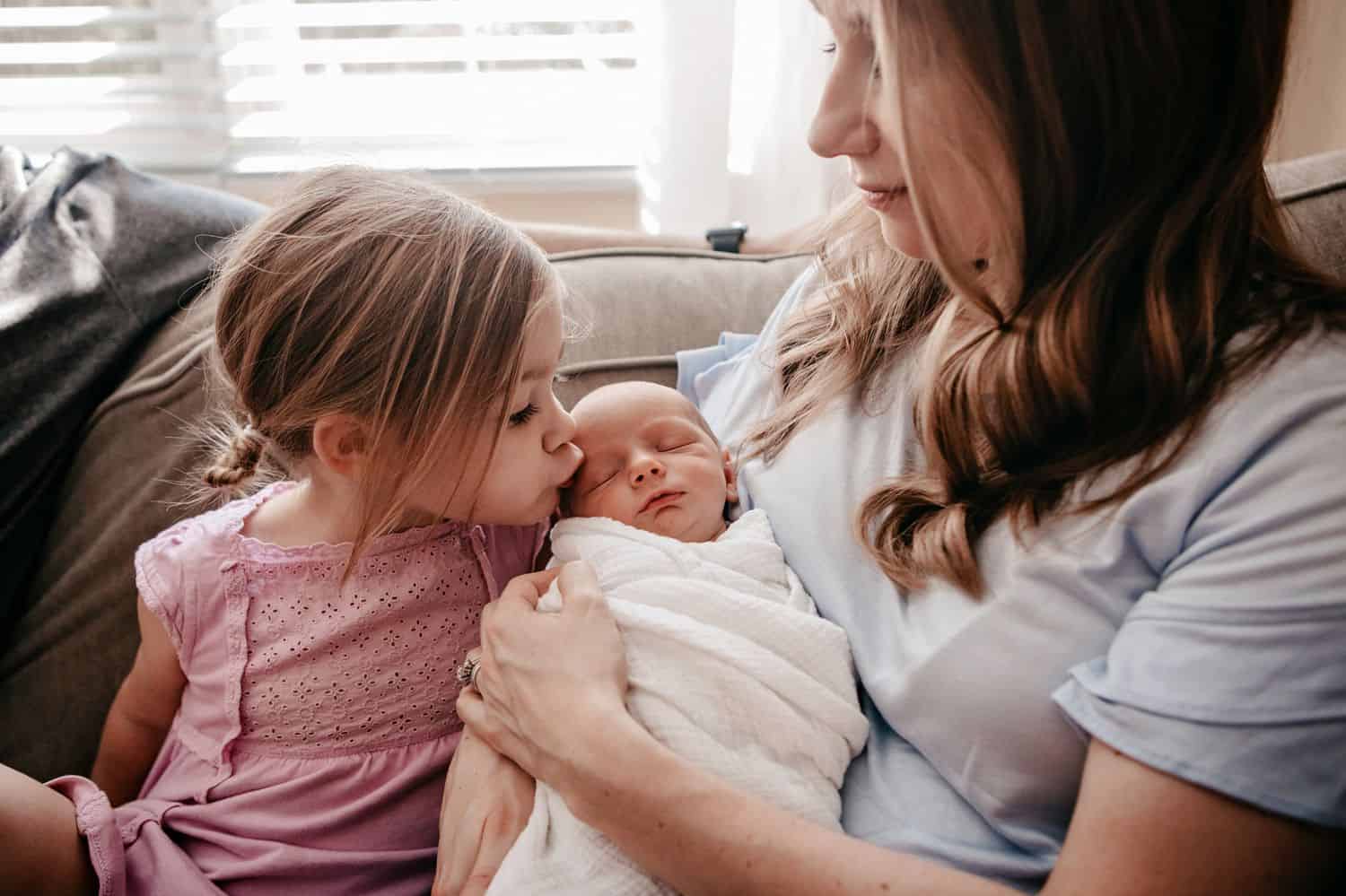 Mom holds her newborn son while his big sister kisses him.
