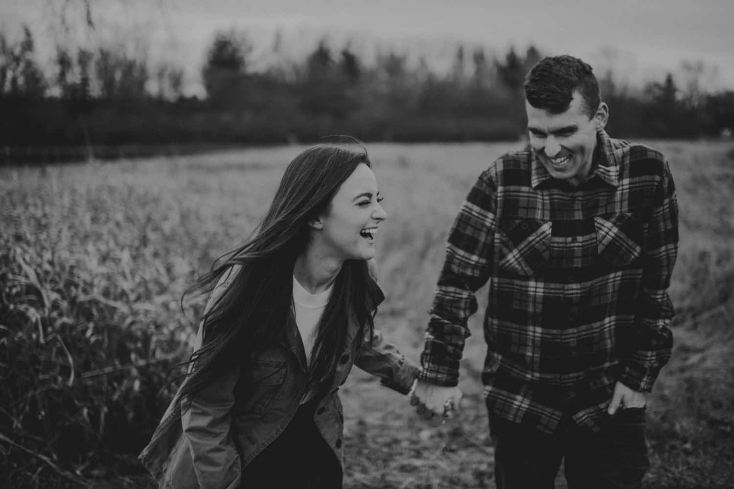 black and white photo of couple laughing and holding hands in a field