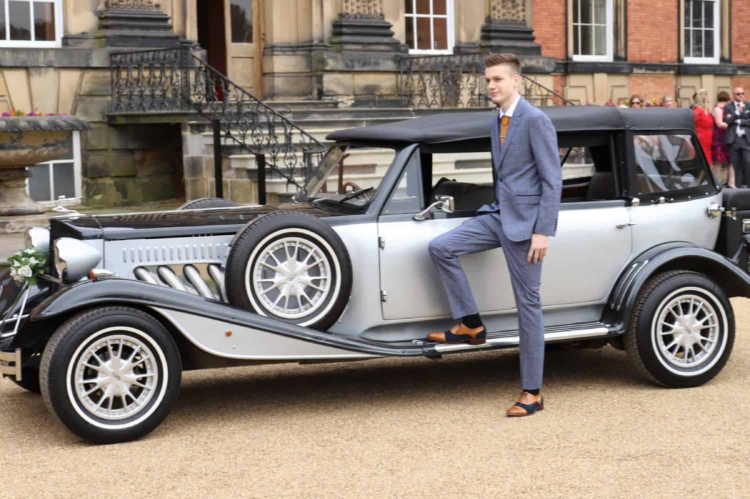A high school senior boy poses for his prom photography beside a vintage car.