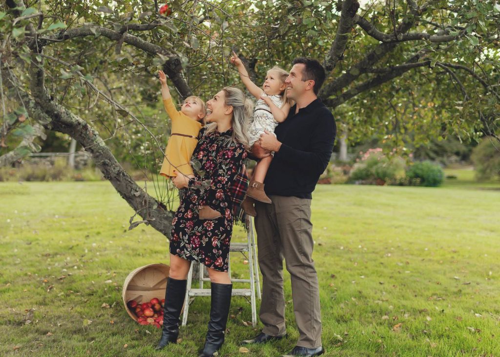 Mariah Gale Creative photographs family photo poses like this, with a family of four picking apples in an orchard.