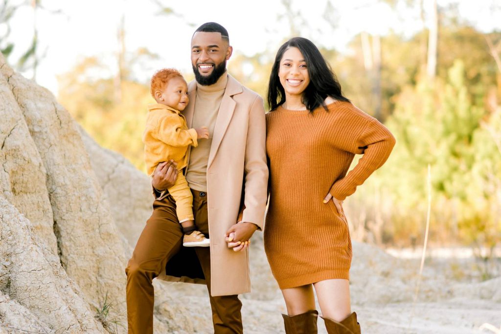 Nyejah Bolds shoots family poses with baby like this one, with a family of three smiling in their orange-gold outfits that stand out against the white desert sand.