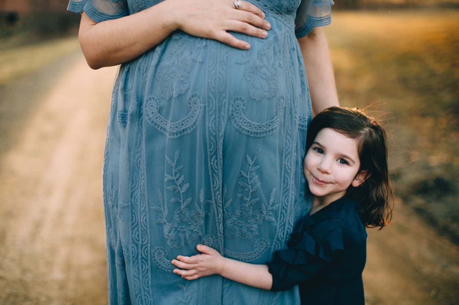 A little girl hugs her pregnant mom's belly.