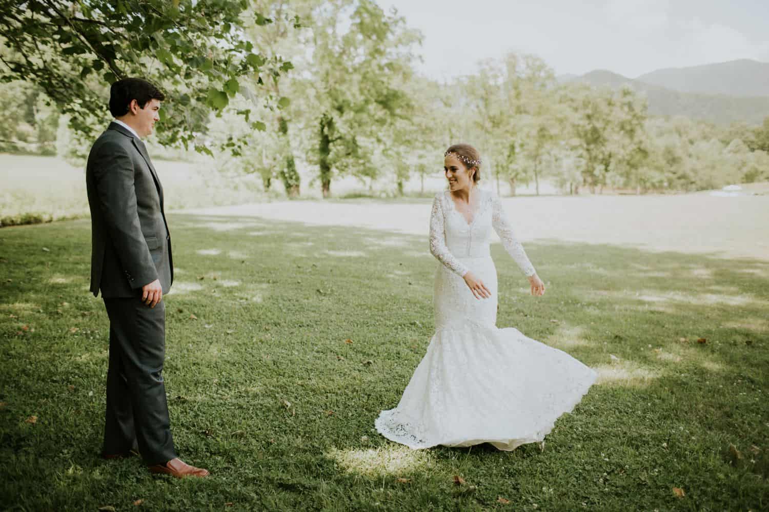 A bride in a long-sleeved lace dress prepares to twirl under a tree during her first look with her husband.
