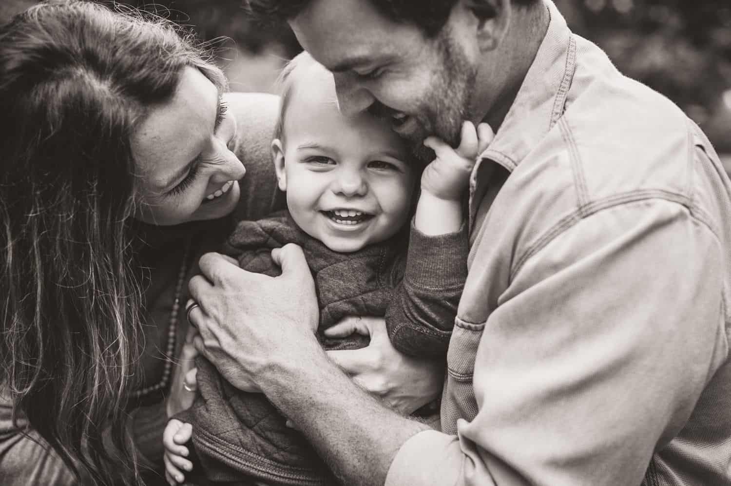 Two parents cuddle close to their toddler in black and white.