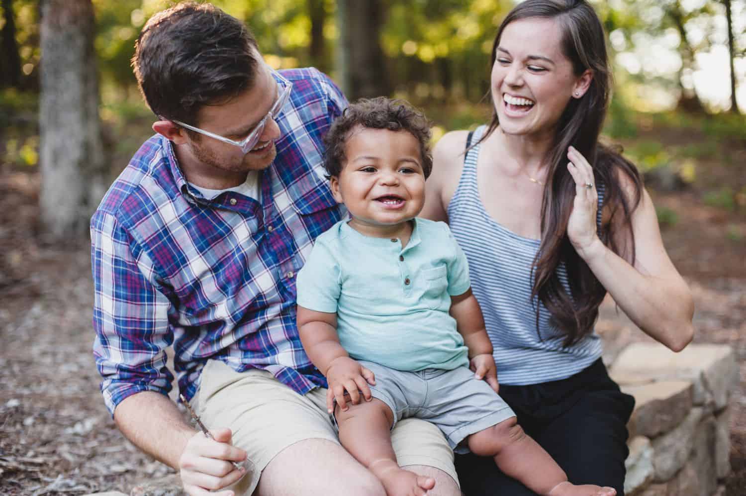 Two parents sit with their smiling toddler in a park.