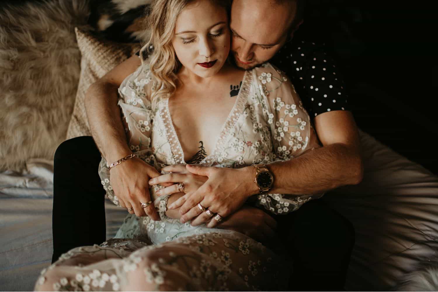 A woman in a white lace dress relaxes into the arms of a man in a black short-sleeved shirt. Learn how to take low light photos like this one by Shelby Laine Photography.