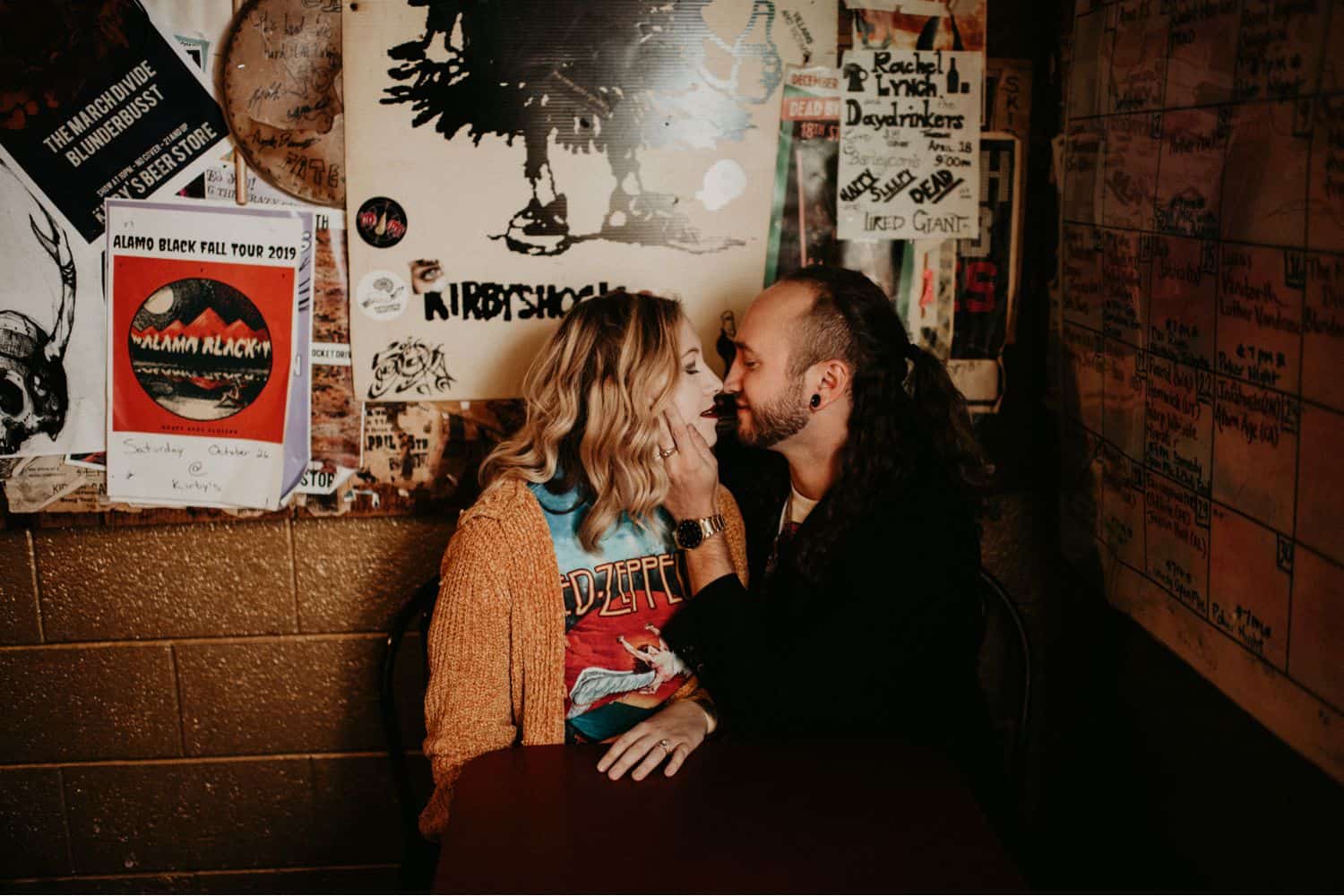Bounce a flash off the wall or ceiling if you aren't sure how to take photos in low lights. In this image, a hipster couple sits in a bar booth kissing. Image by Shelby Laine Photography