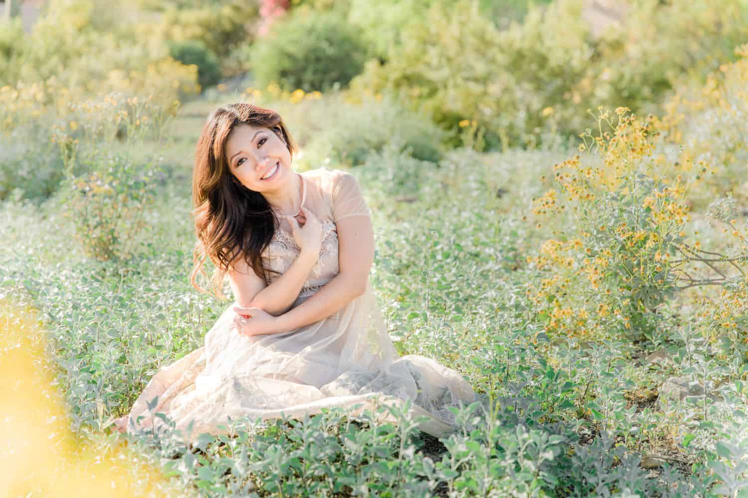 A pregnant mother sits sweetly in an overgrown field full of wildflowers