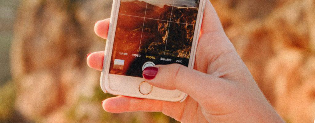 A woman's hand holding an iPhone and taking a picture of the coastal landscape
