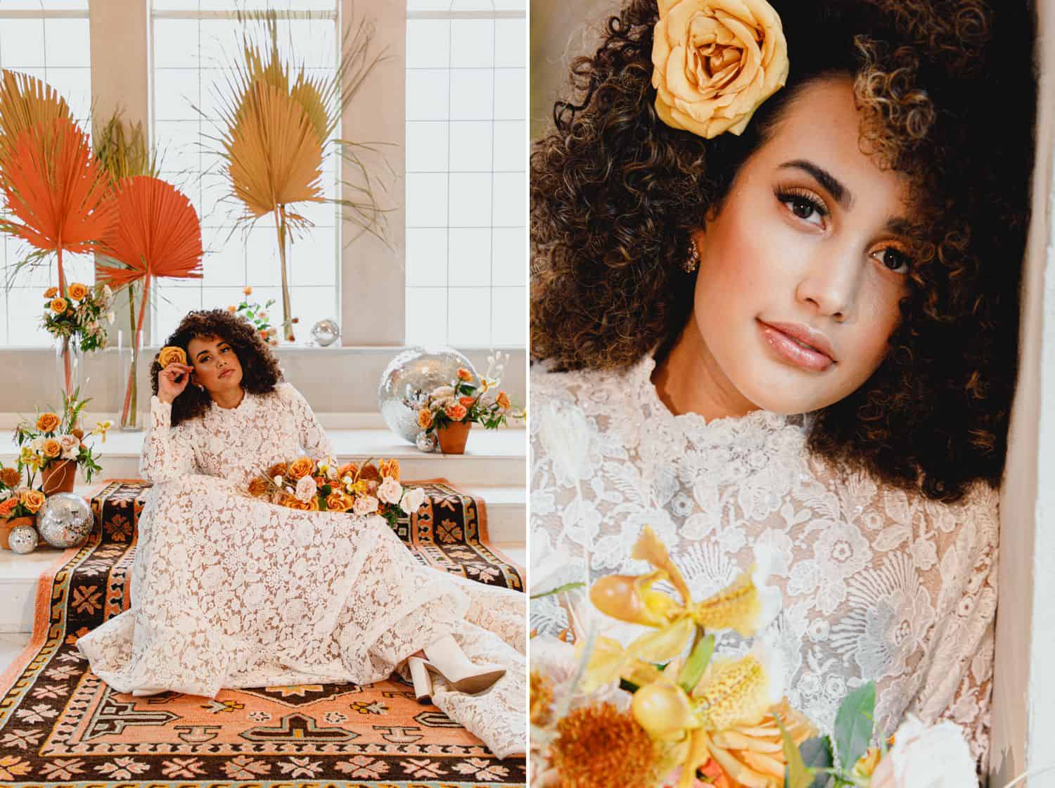 A bride in a high neck lace dress poses on a Moroccan rug in a room with huge windows decorated with orange and yellow roses.