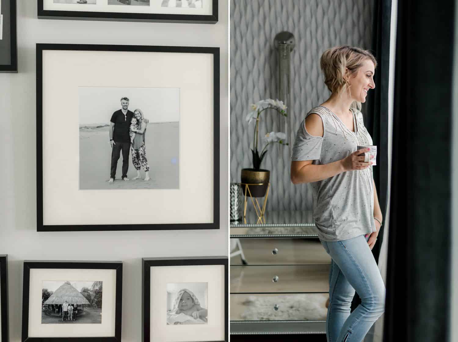 Black and white prints cover a home's wall. A woman stands at the window holding a cup of coffee.