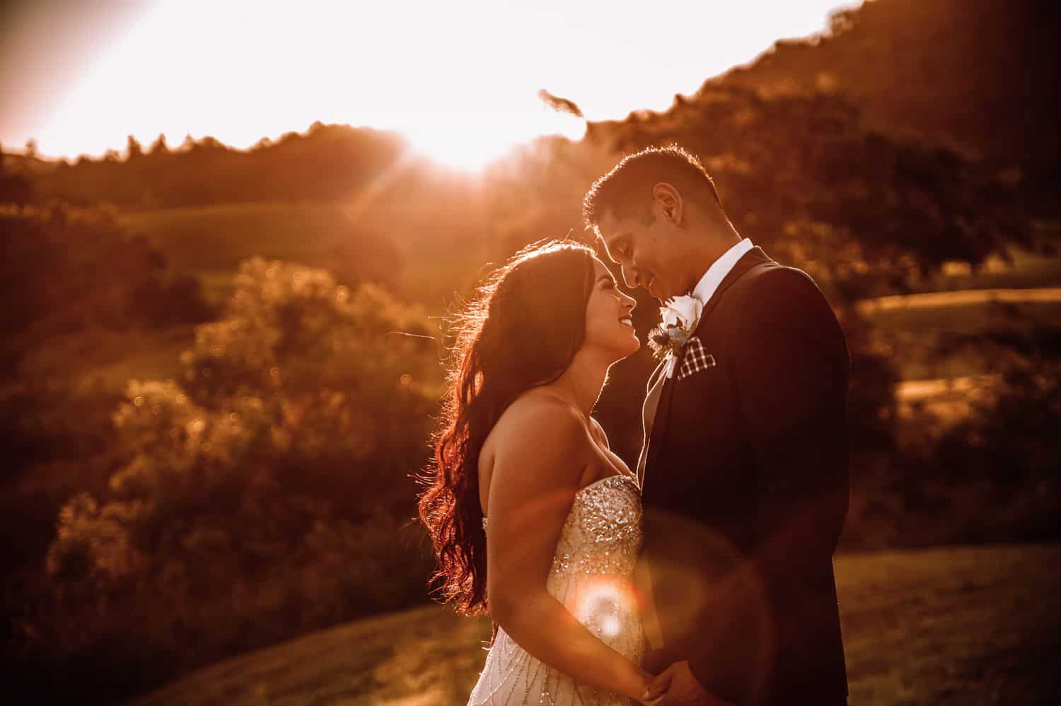 Bride and groom hold hands facing each other with the sun setting behind them.