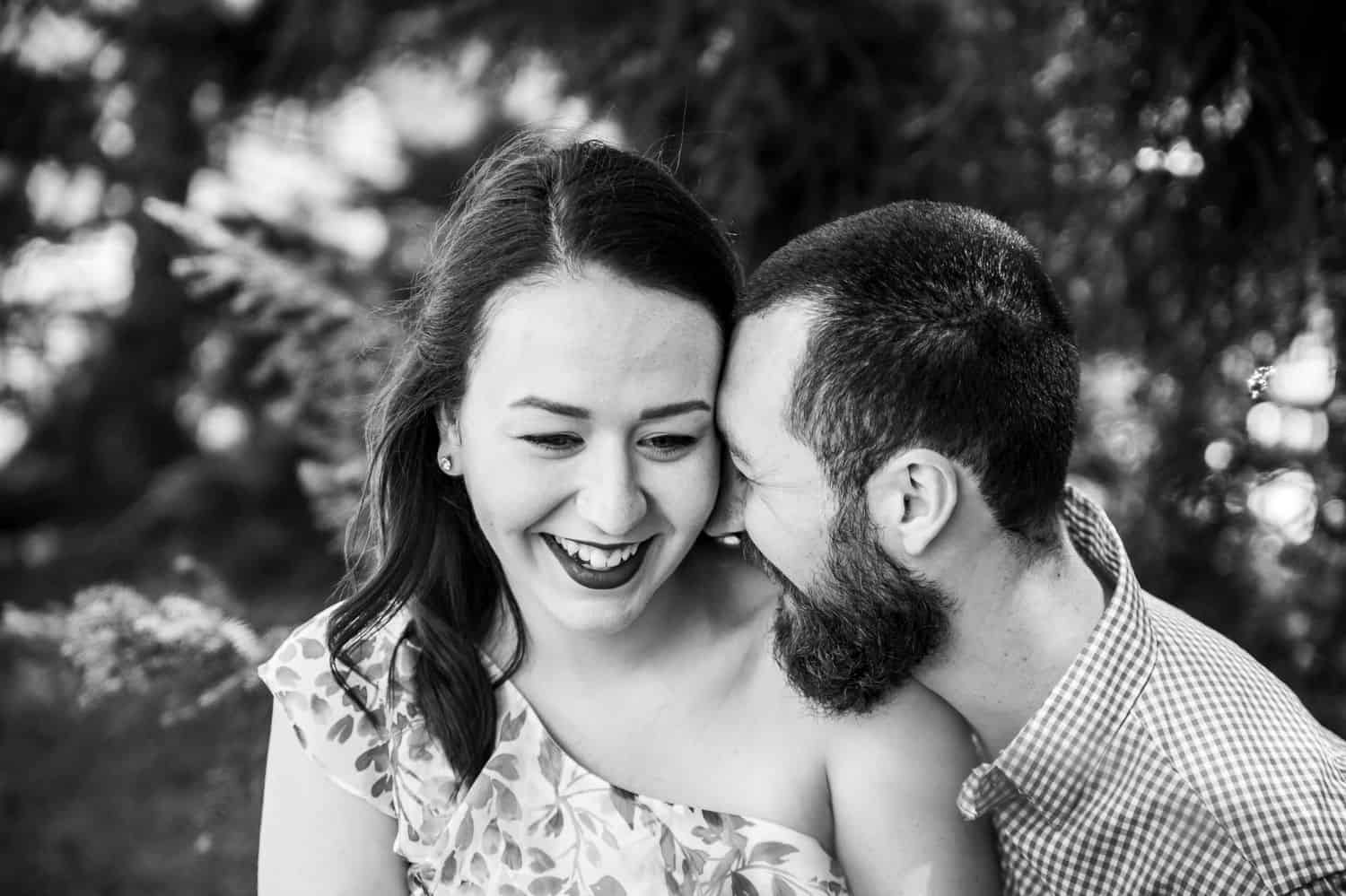 Black and white photo of man leaning his forehead against his girlfriend’s cheek as they both smile.