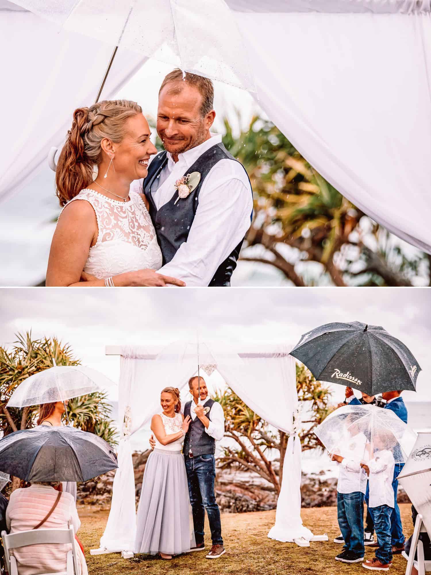 Bride and groom in the rain in front of curtained archway with a clear plastic umbrella held over them. Bride and groom in the rain in front of a curtained archway surrounded by guests with umbrellas.