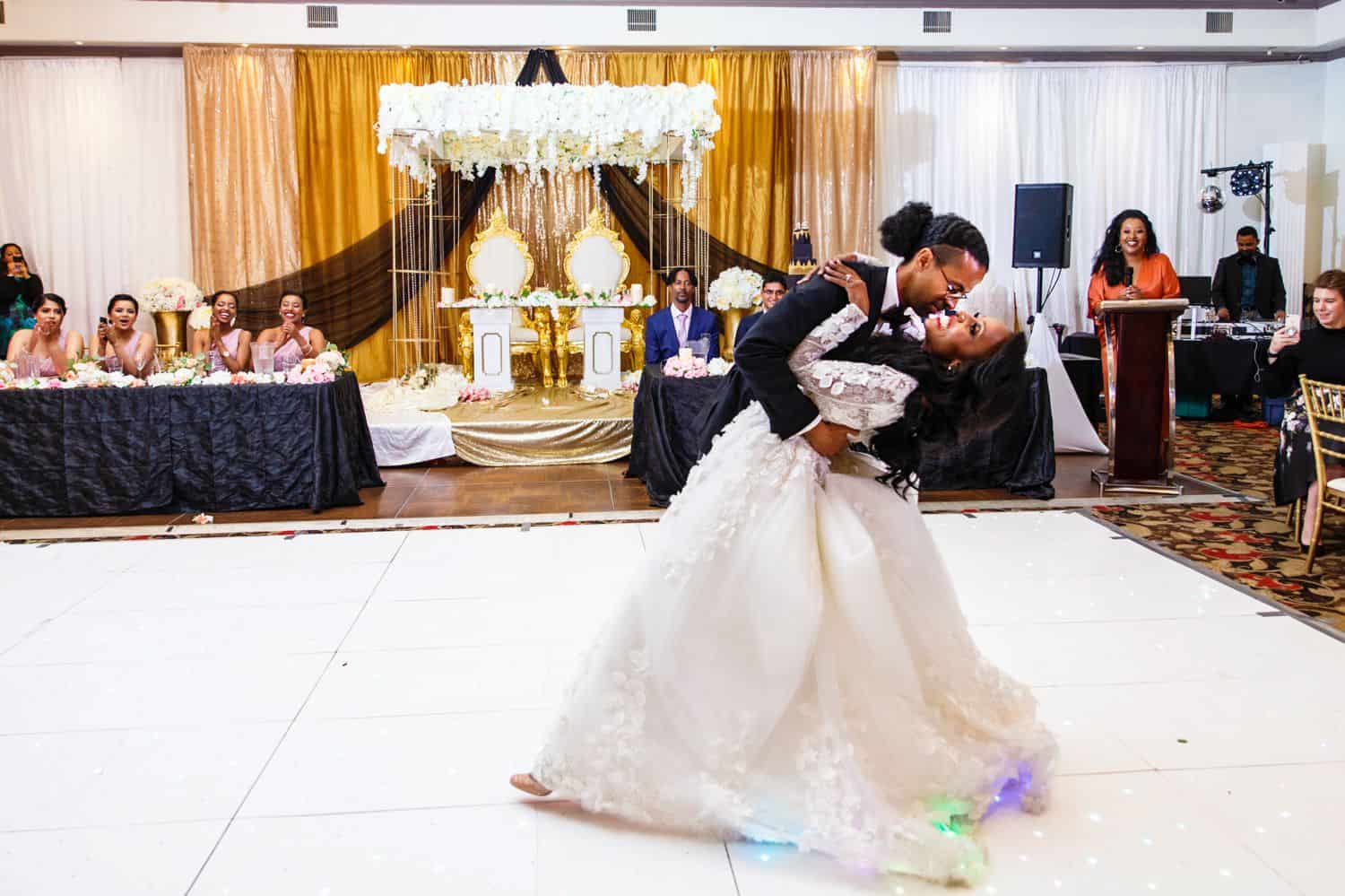 A groom dips the bride during their first dance in a ballroom