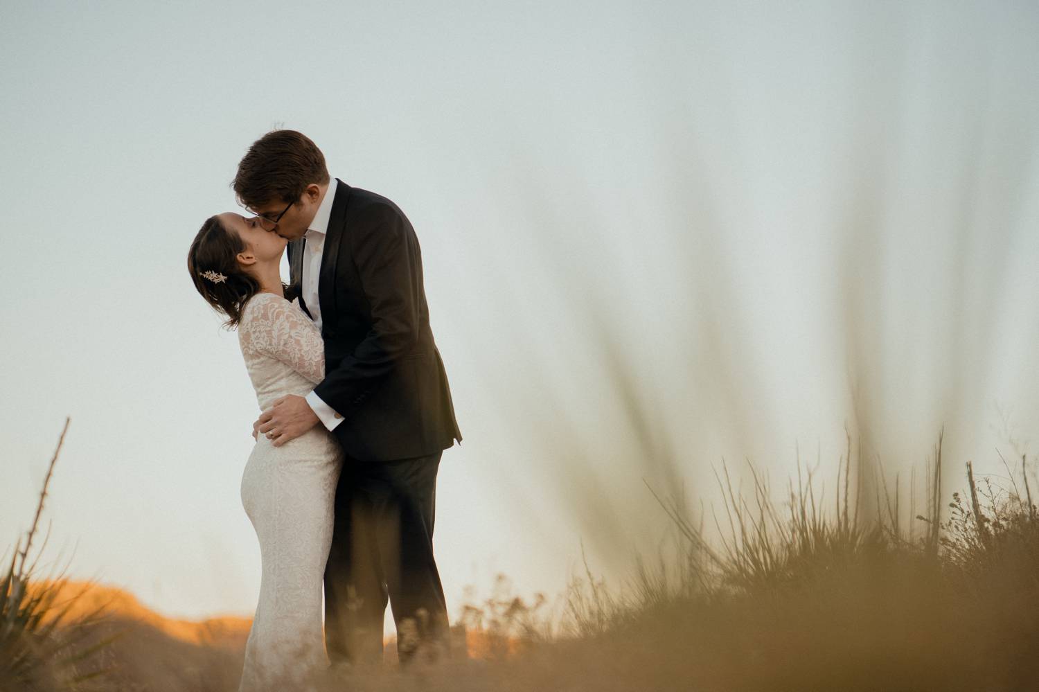 Customer Loyalty: By Nick Sparks, a bride and groom kiss at twilight in the middle of a wheat field.