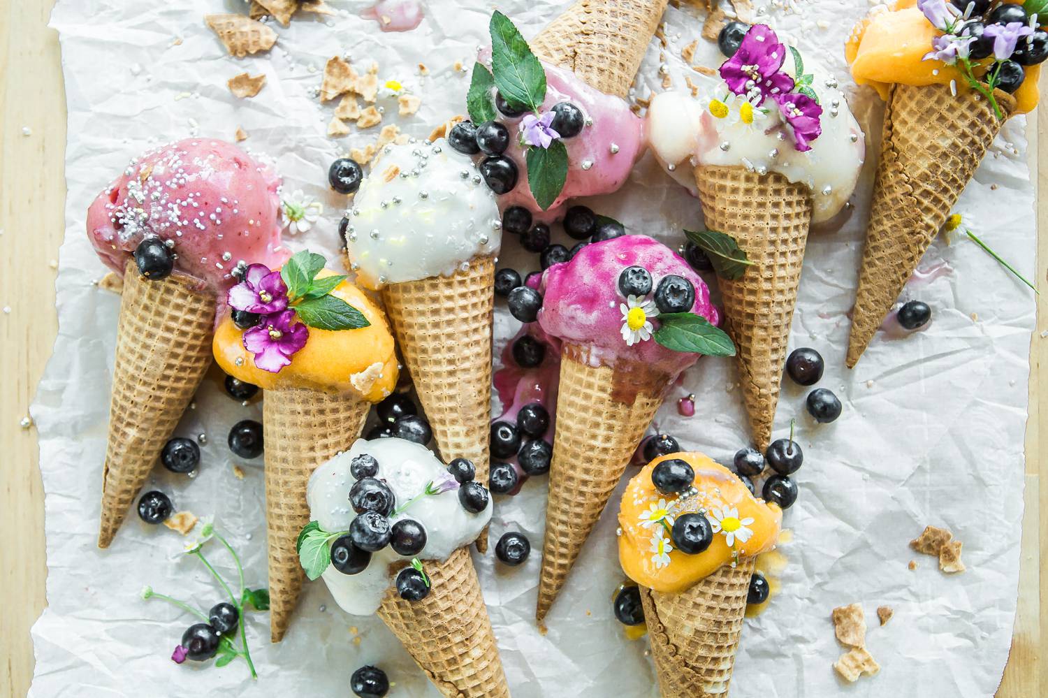 Colorful ice cream cones are displayed on a marble slap and covered with berries and mint sprigs