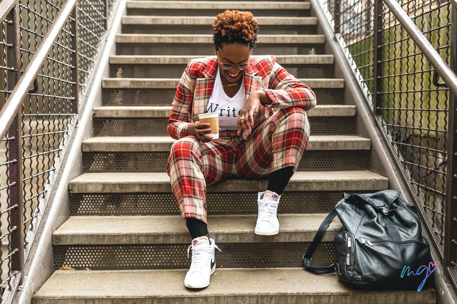 Photo: Mecca Gamble's personal branding portrait of a writer shows the woman wearing a red plaid suit over a t-shirt that says, "Writer". She's sitting on a set of concrete steps, holding a coffee cup, and laughing as she looks down toward her white Nikes.