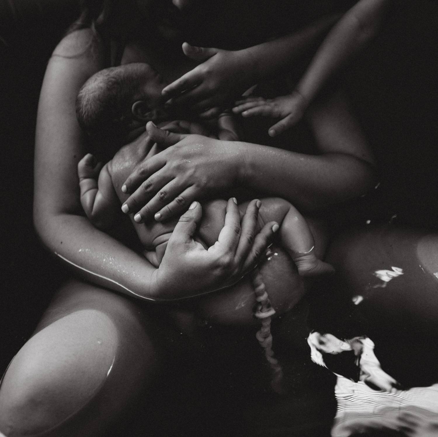 A new mother clutches her newborn baby to her chest as she rests in a tub of water
