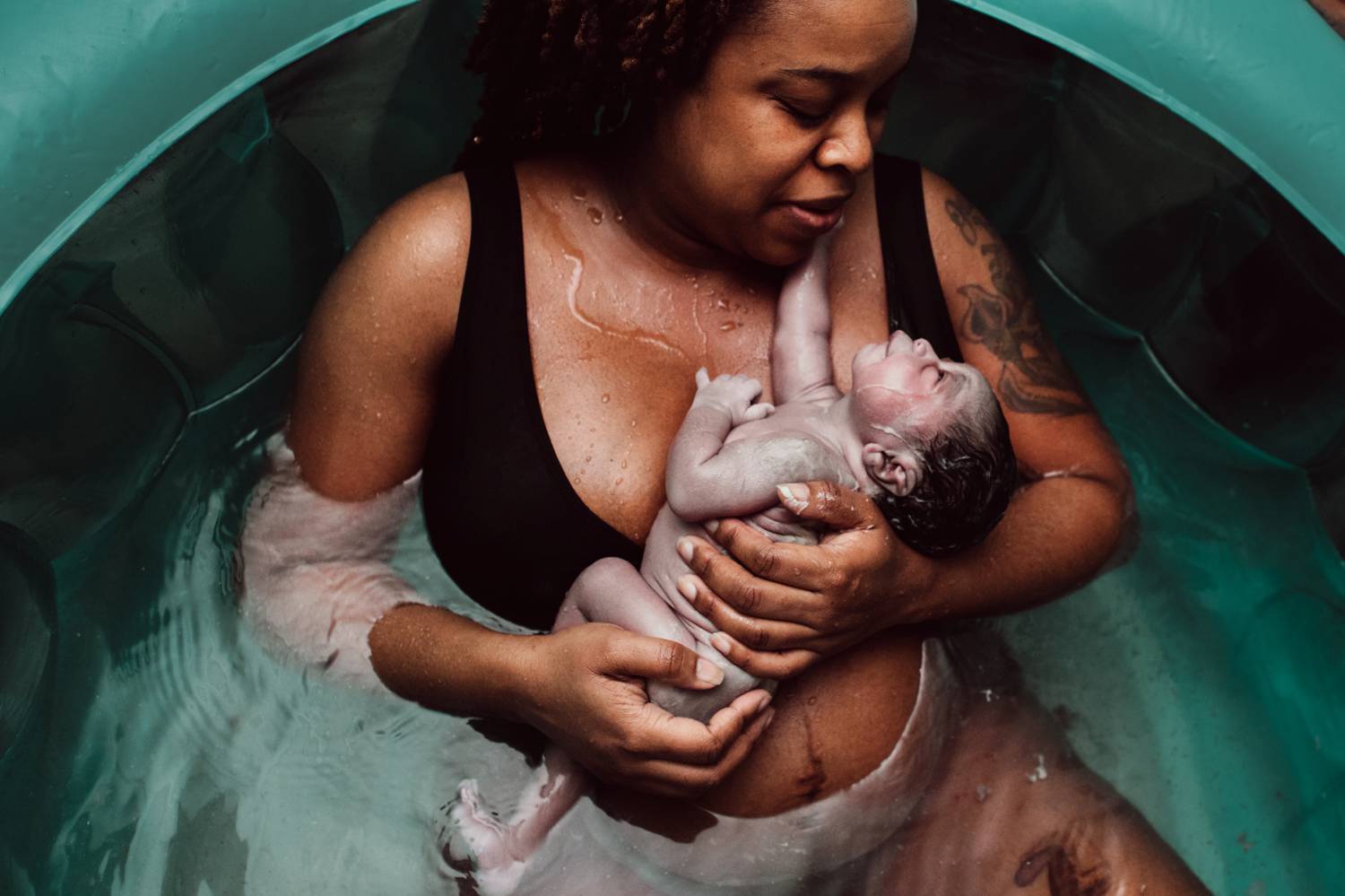 A new mother reclines in an inflatable bath holding her newborn baby against her chest