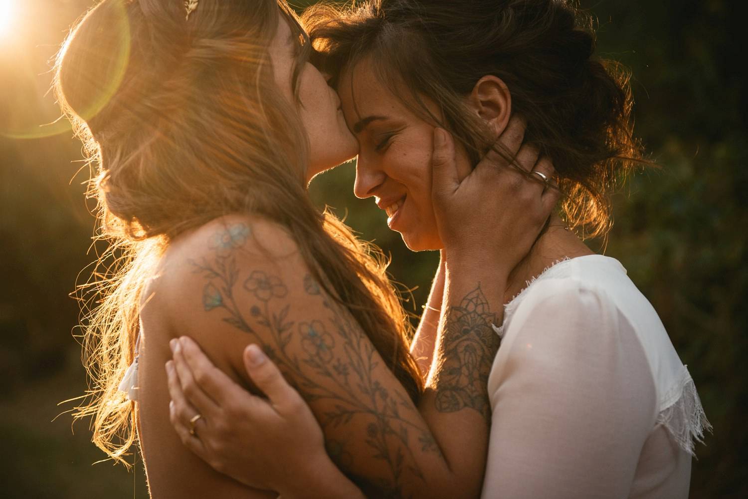 One bride kisses her new wife on the forehead as golden sunlight spills across them