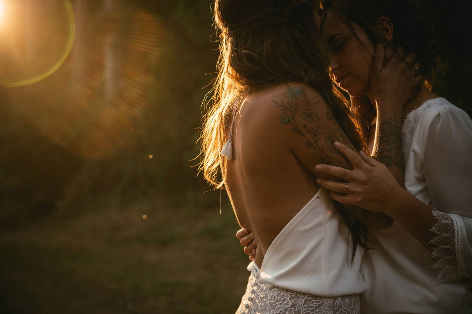 Two brides hold eachother close as the setting sun bathes their skin in warm light.