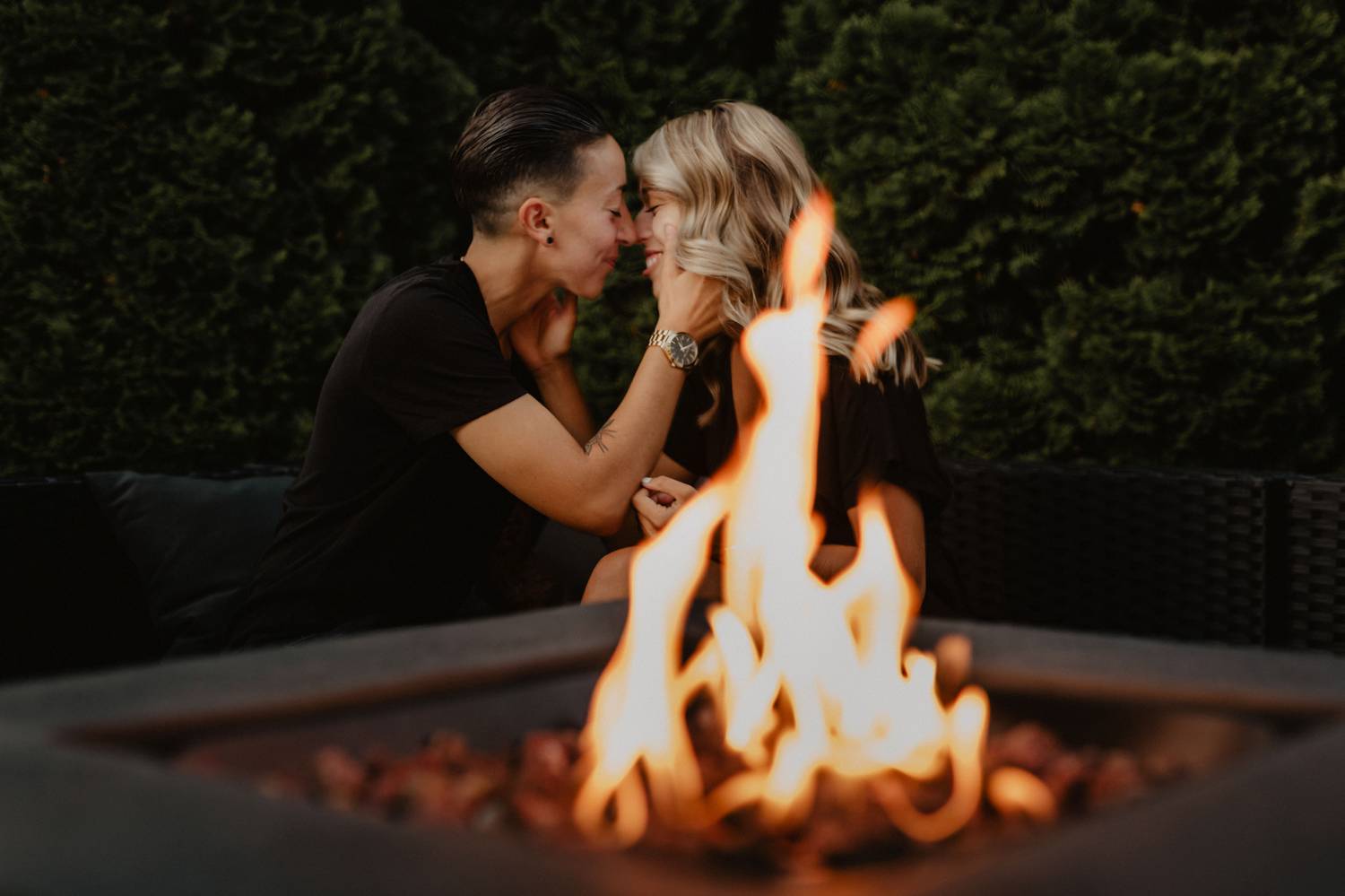 An LGBTQ couples move in close to kiss as they're photographed across the flames of a twilight fire pit