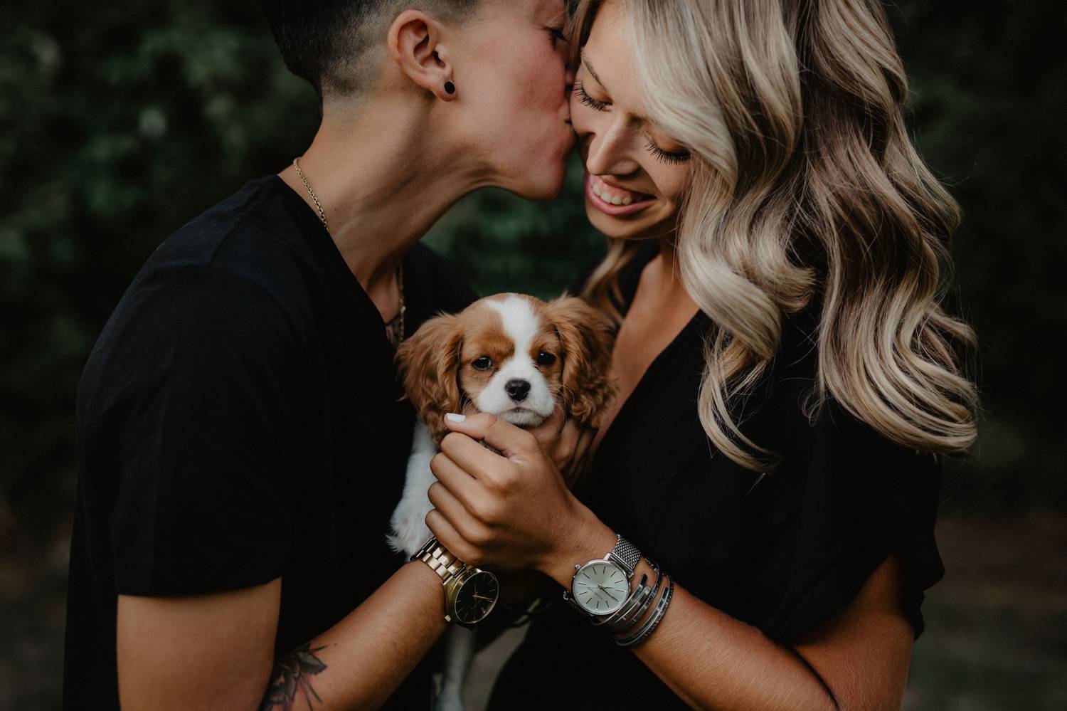 One partner kisses the other on the cheek in this twilight LGBTQ engagement shoot