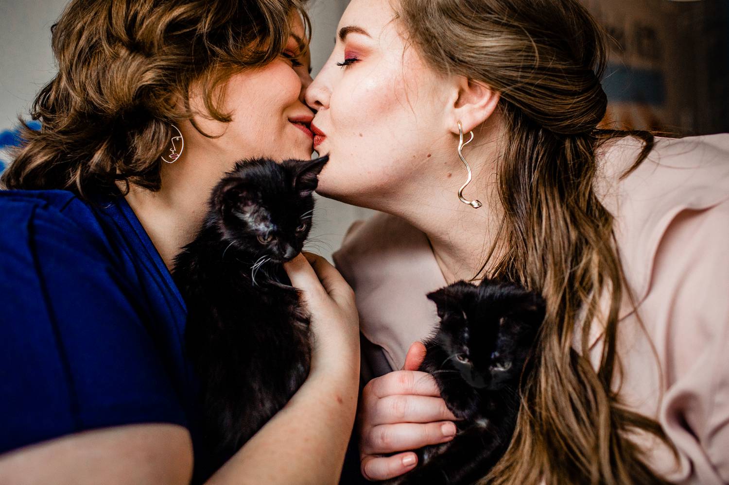 Two women kiss while smiling and holding cuddly kittens during their engagement photos