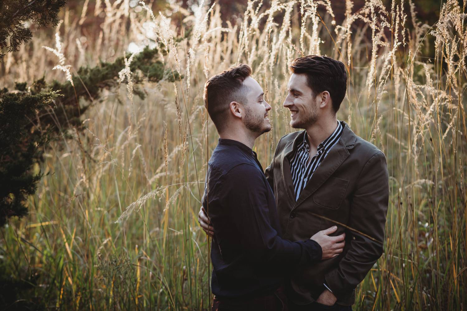 Two men pose for engagement photos in a grassy field
