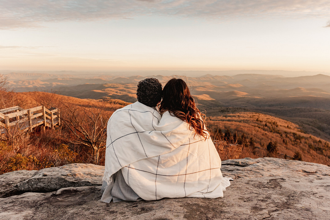Engagement photograph of couple sitting on a rock overlooking scenery