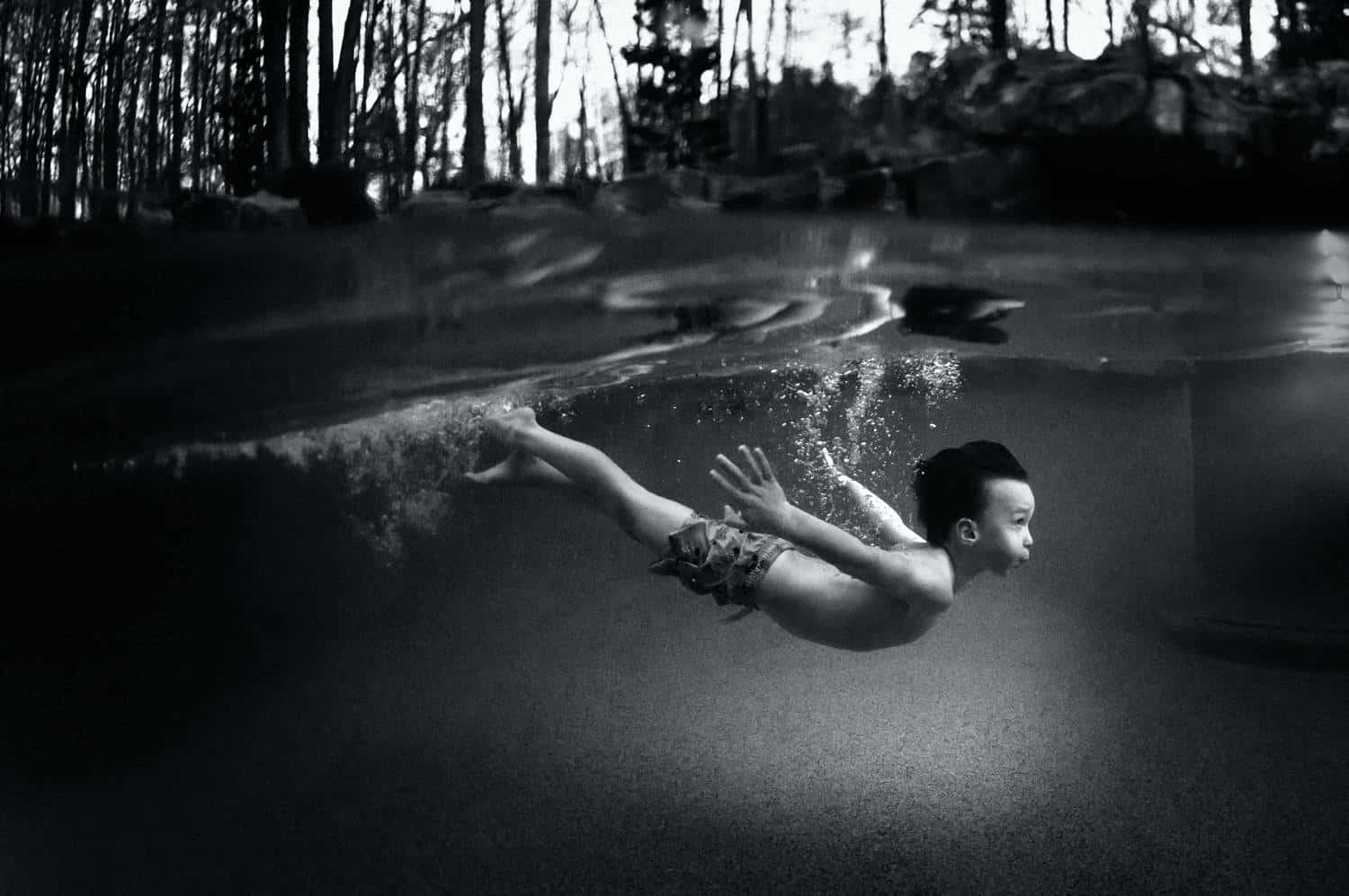 A black and white photographs of a child swimming underwater at dusk