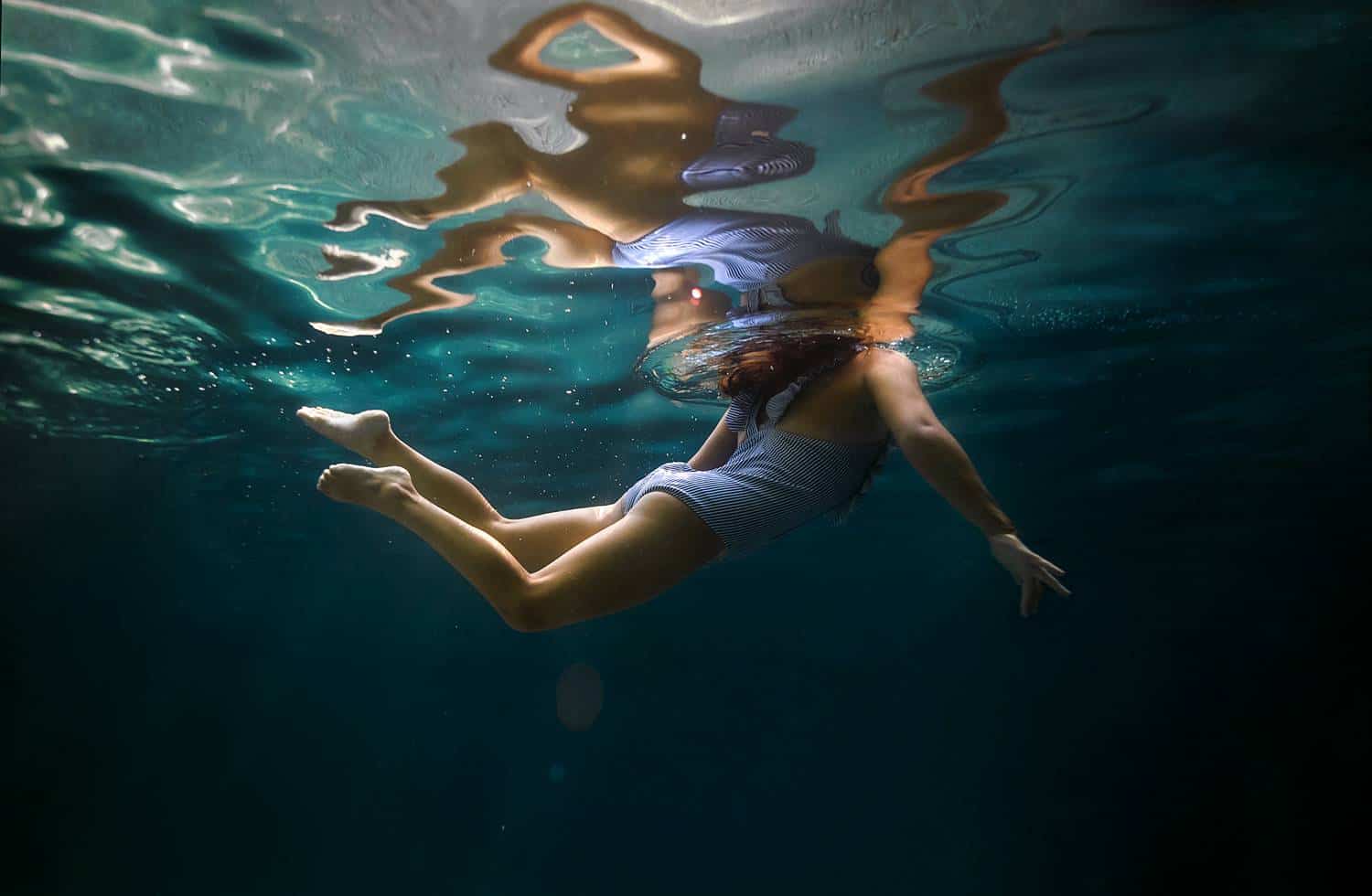 A child in a blue bathing suit swims with their head barely breaking the surface of the pool