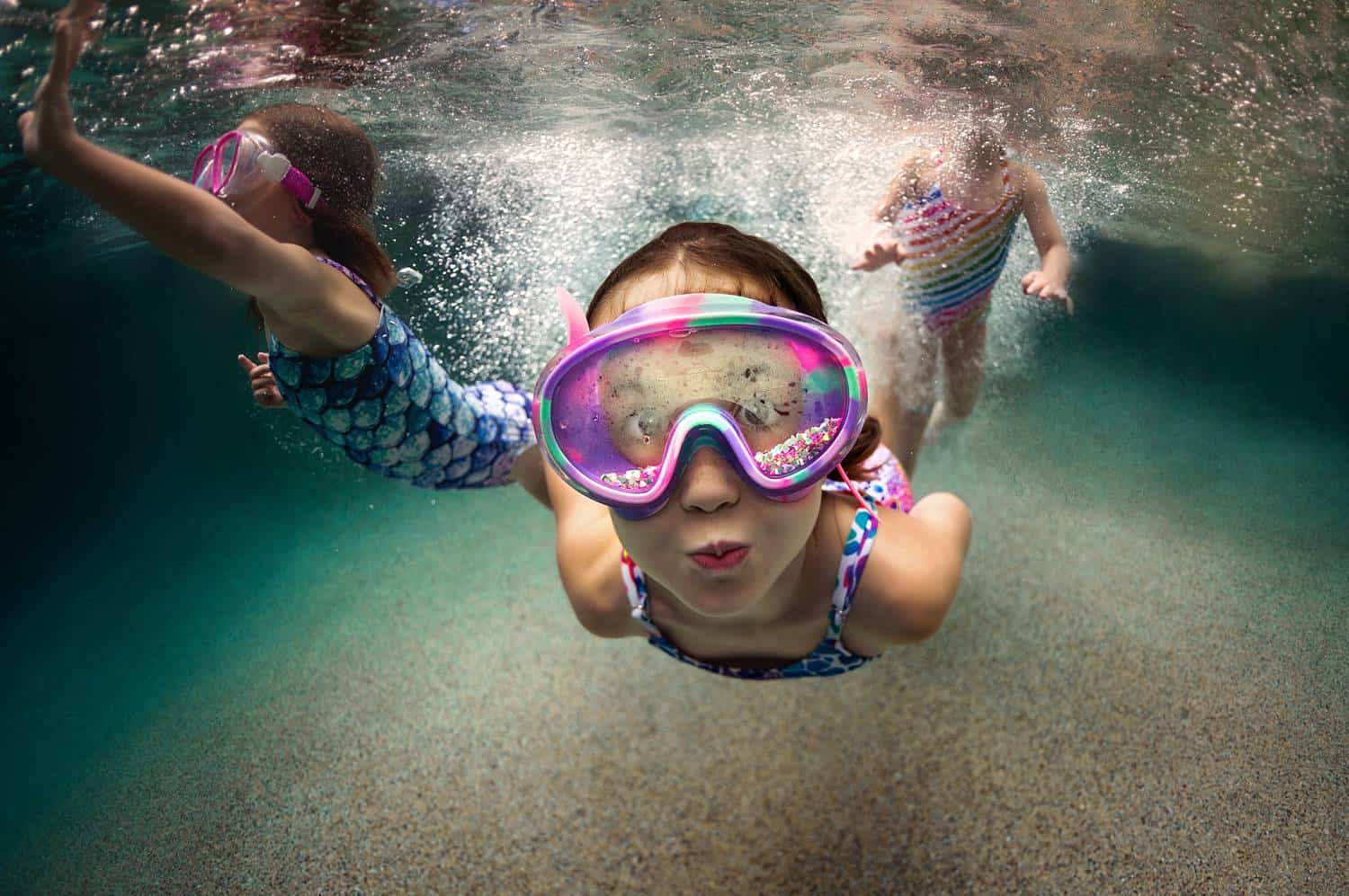 A child wearing oversized purple goggles swims toward the camera