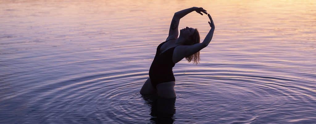A dancer with chronic pain poses for a photograph in a still lake