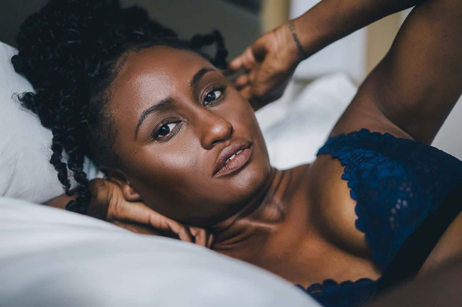 A Black model in blue lingerie poses for photographer Toni Black during a boudoir session on a white bed