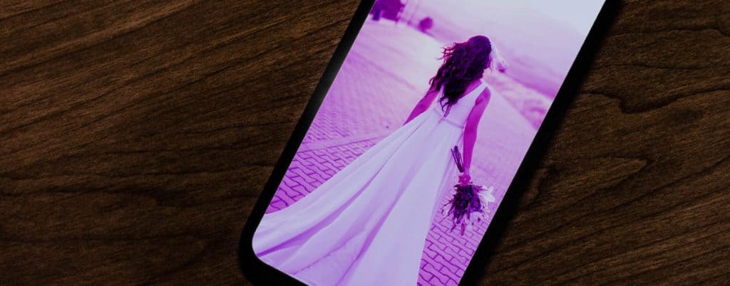 On the left is the original photograph of a bride photographed from behind. She is standing on a cobblestone street facing the warm mountain sunset while her dress billows behind her. In the second photo, the bride's image is displayed on an iPhone where it has been overlayed with a fushia filter.