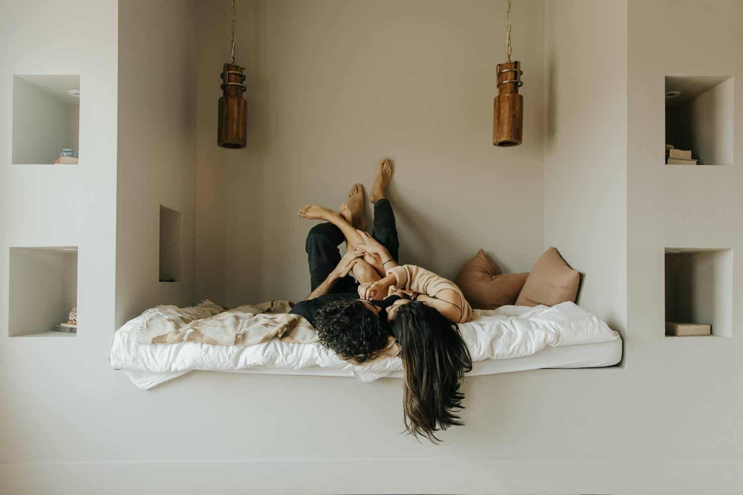 A couple lounges together in an alcove bed, their arms and legs wrapped around eachother in a moment of passion. Learn how to take boudoir photos like this one by reading the ShootProof blog!