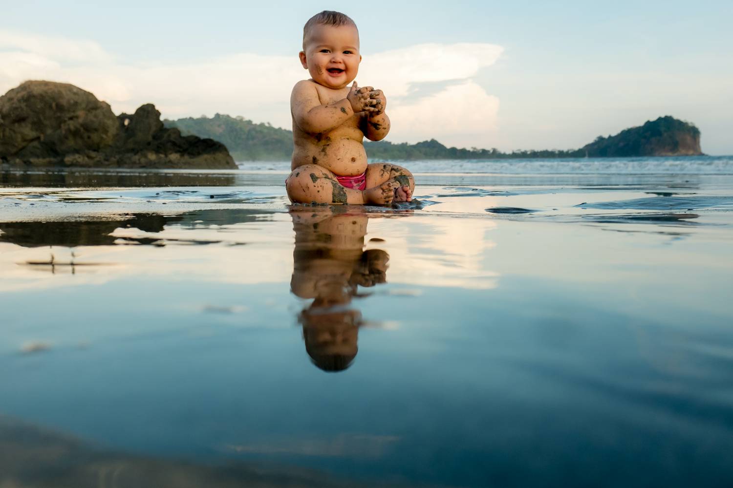 Customer Experience: A photo by Kevin Heslin depicts a baby sitting on a beach surrounded by reflective puddles of water.