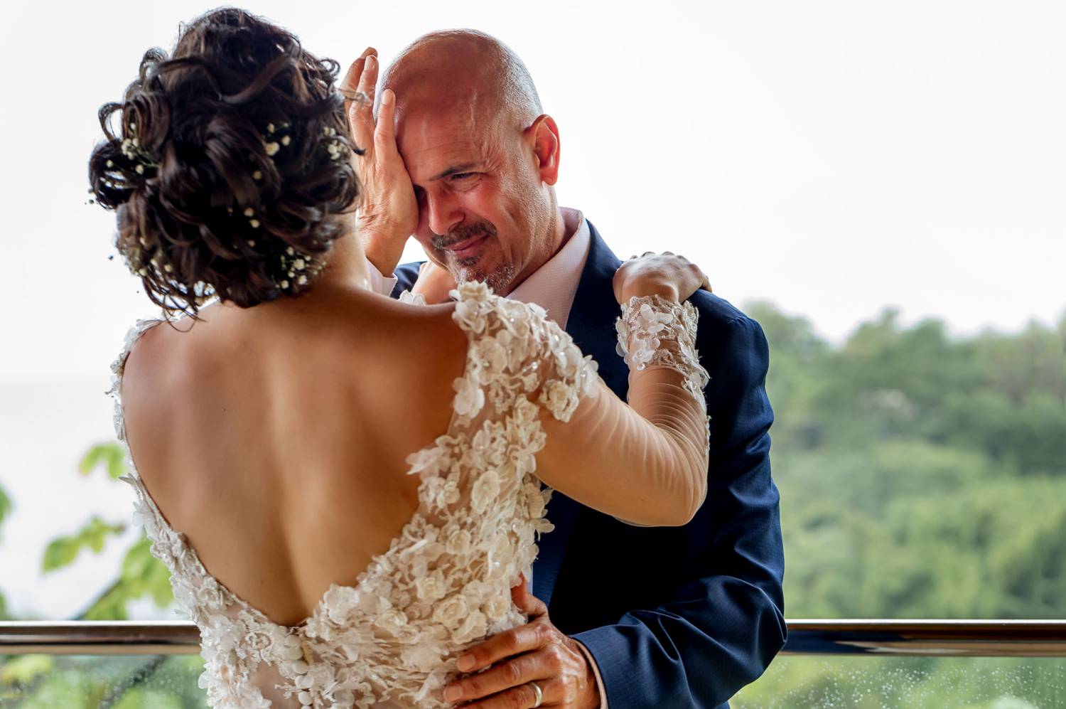 A photo by Kevin Heslin depicts a groom wiping tears away as his new wife wraps her arms around his shoulders.