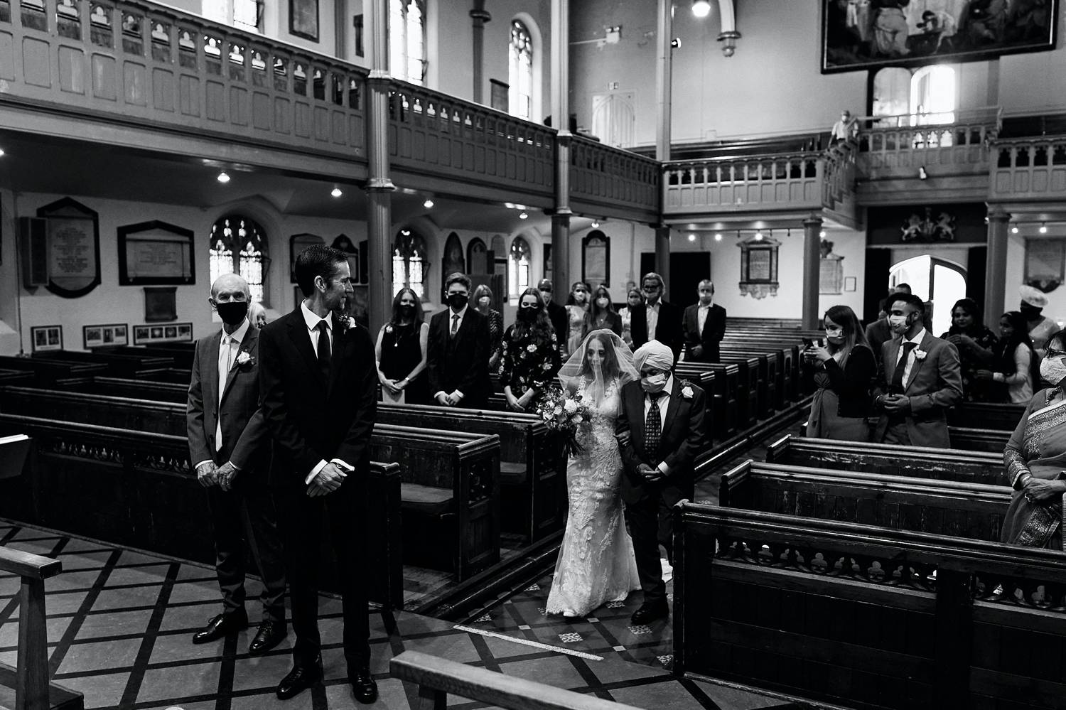 2020 Photographers are Resilient: a black and white photograph of a bride entering the church with her father, who wears a face mask.