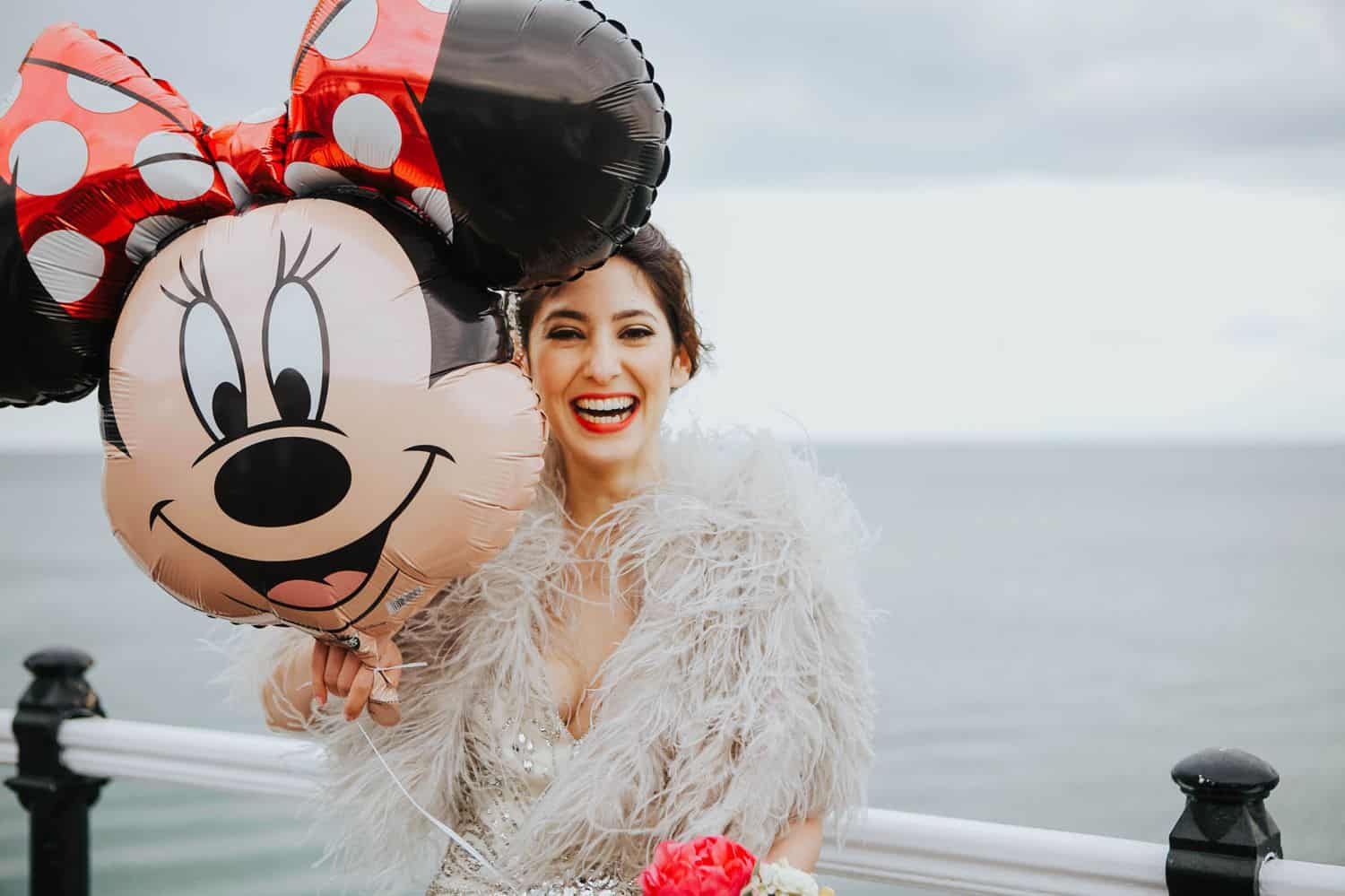 How To Make A Photography Website Your Dream Clients Can’t Resist: a bride draped in feathers holds a Minnie Mouse balloon in front of an expansive ocean scene.