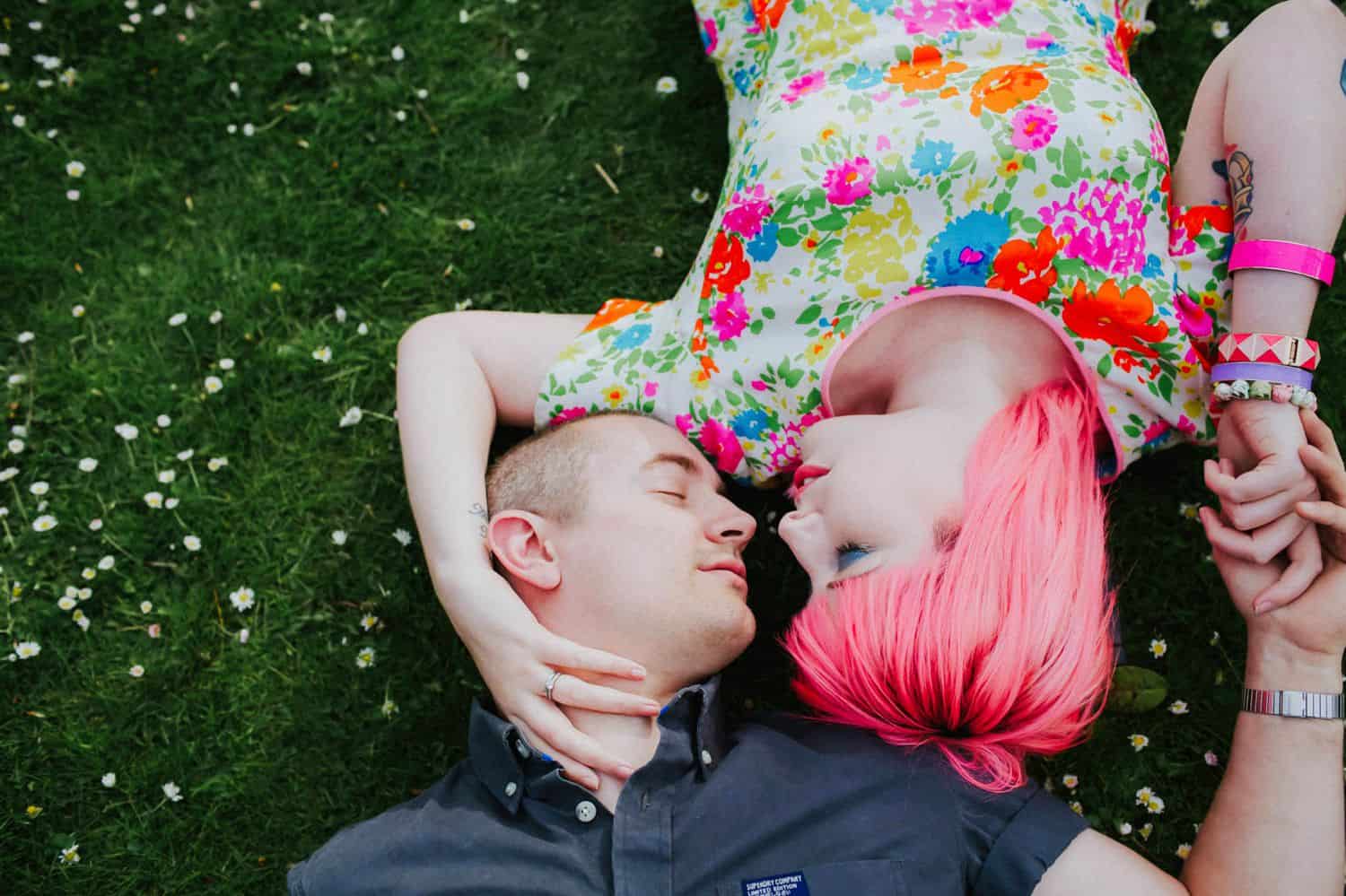 How To Make A Photography Website Your Dream Clients Can’t Resist: A pink-haired woman and her partner lie face-to-face in the grass holding hands.