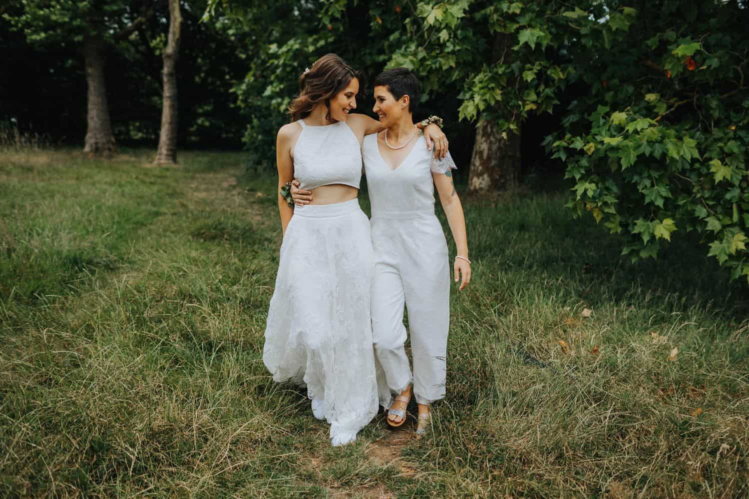 How To Make A Photography Website Your Dream Clients Can’t Resist: Two brides walk through the woods with their arms wrapped around each other.